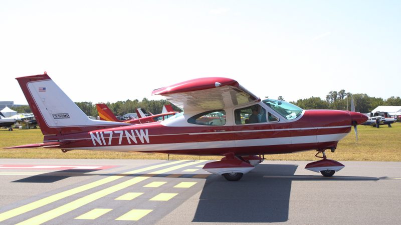 Red and white single-engine Cessna 177A Cardinal taxiing on an airport ramp, side view.