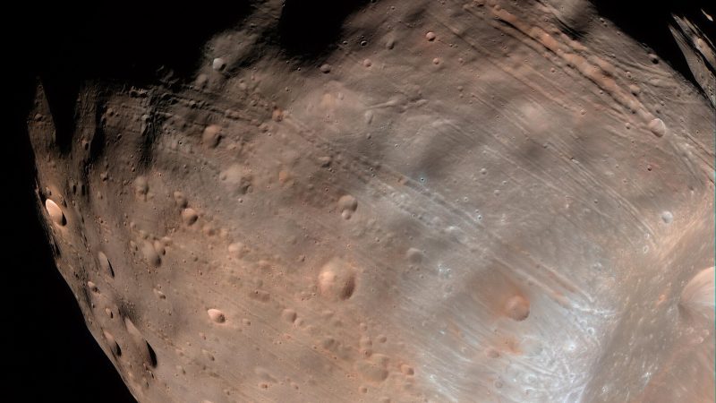 Color view of Phobos, a potato-shaped, heavily cratered moon, with the large crater Stickney at lower right against black space.
