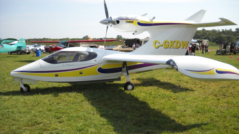White amphibious Seawind single-engine aircraft with colored stripes parked on grass at an airshow.